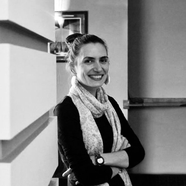 Ani Haykuni, founder of Global Founder Lab A woman with a scarf smiles while standing against a wall in a cafe setting.